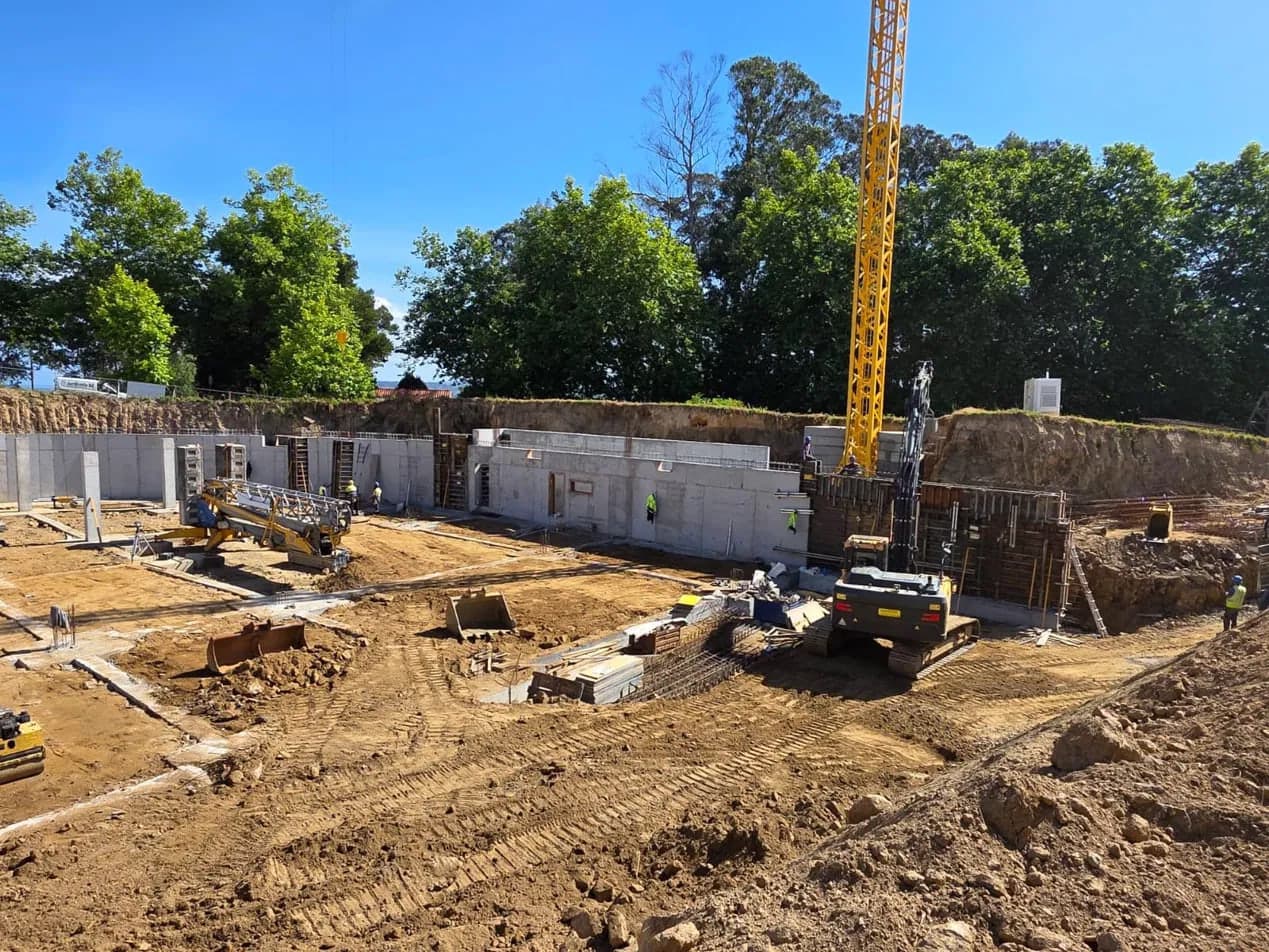 Site at foundation stage with reinforced concrete basement walls and a tower crane