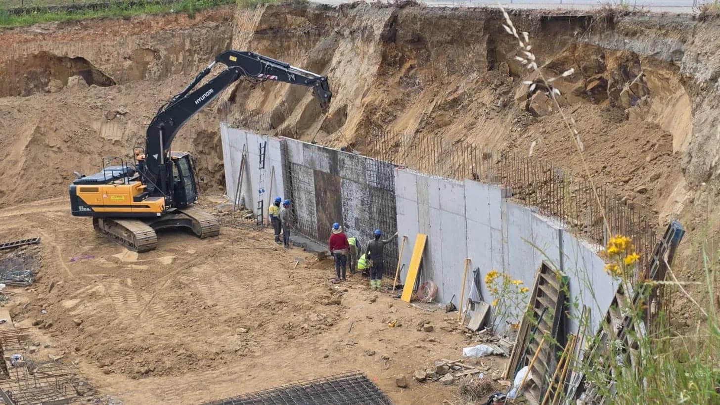 Muro de contención de hormigón armado en ejecución dentro de una excavación, con operarios y encofrados
