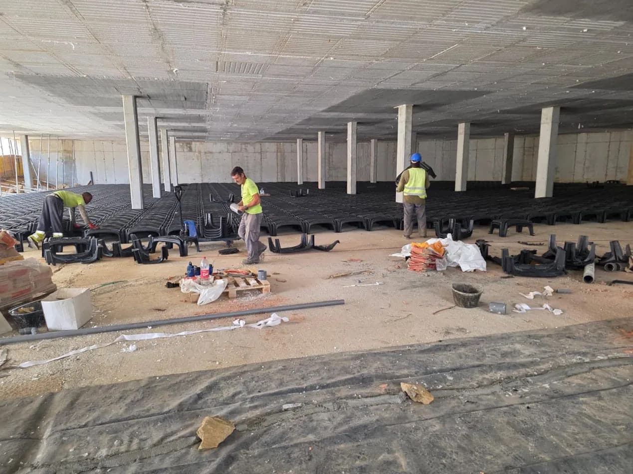 Workers placing modular permanent formwork for a ventilated ground slab between reinforced concrete columns