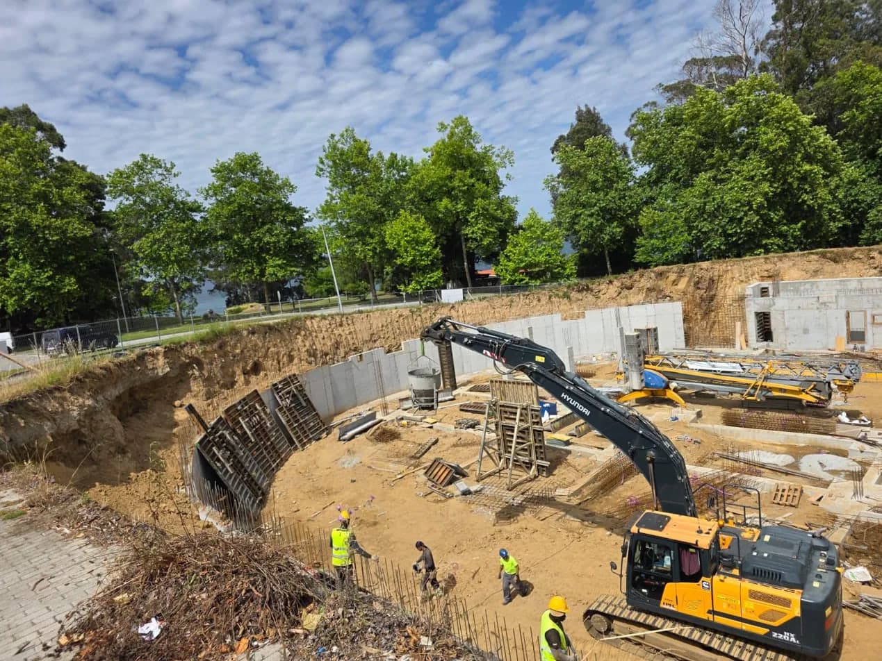 Excavación con muros curvos de hormigón armado, paneles de encofrado y operarios en obra
